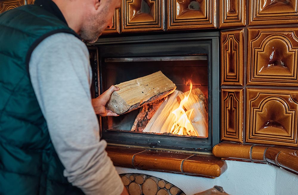 Man Putting fire Wood Logs In The Home Mantel Fire.