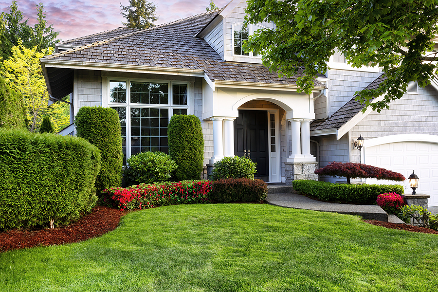 Beautiful home exterior in evening with manicured green lawn and blooming red flowers in bushes